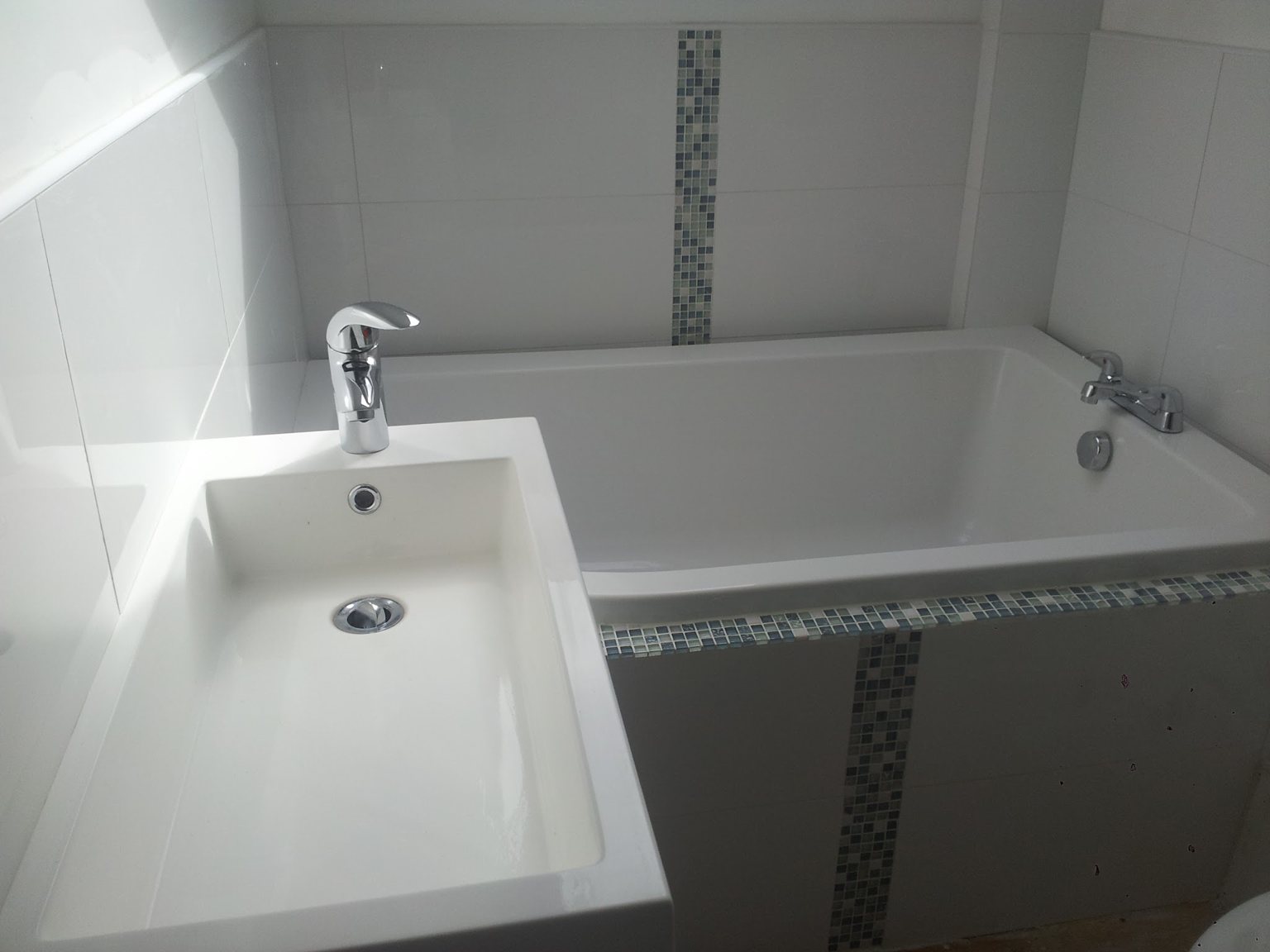 White bathroom with a mosaic strip running round the walls and across the bath panel