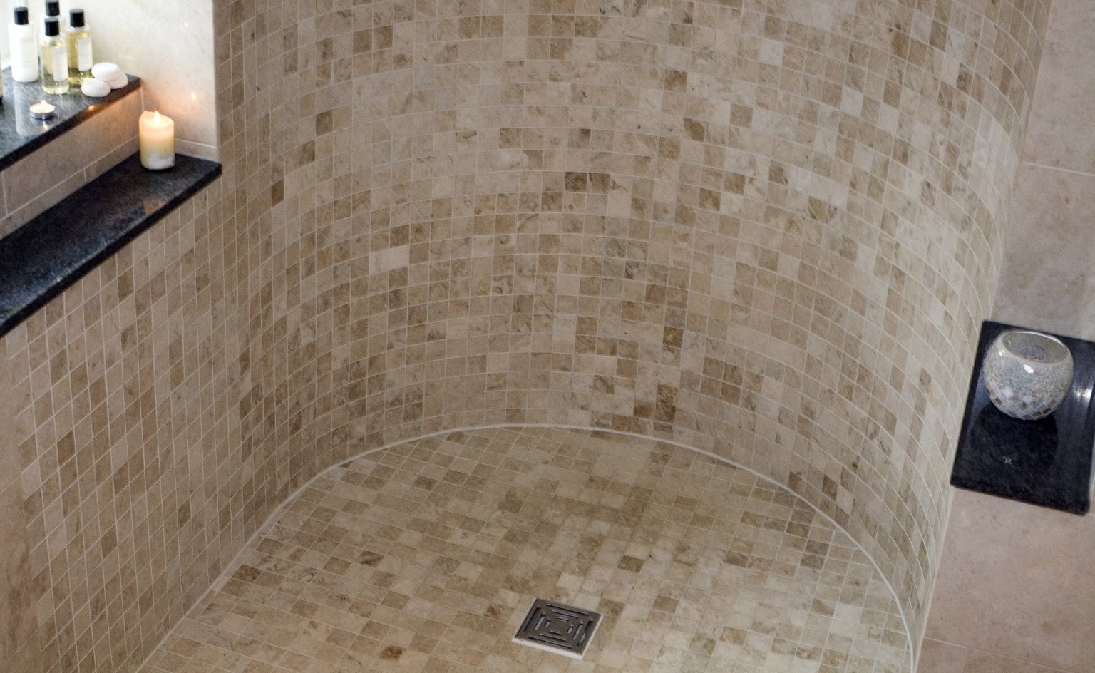 Curved walk-in shower tiled in travertine mosaic with a tiled floor sweeping into the shower area
