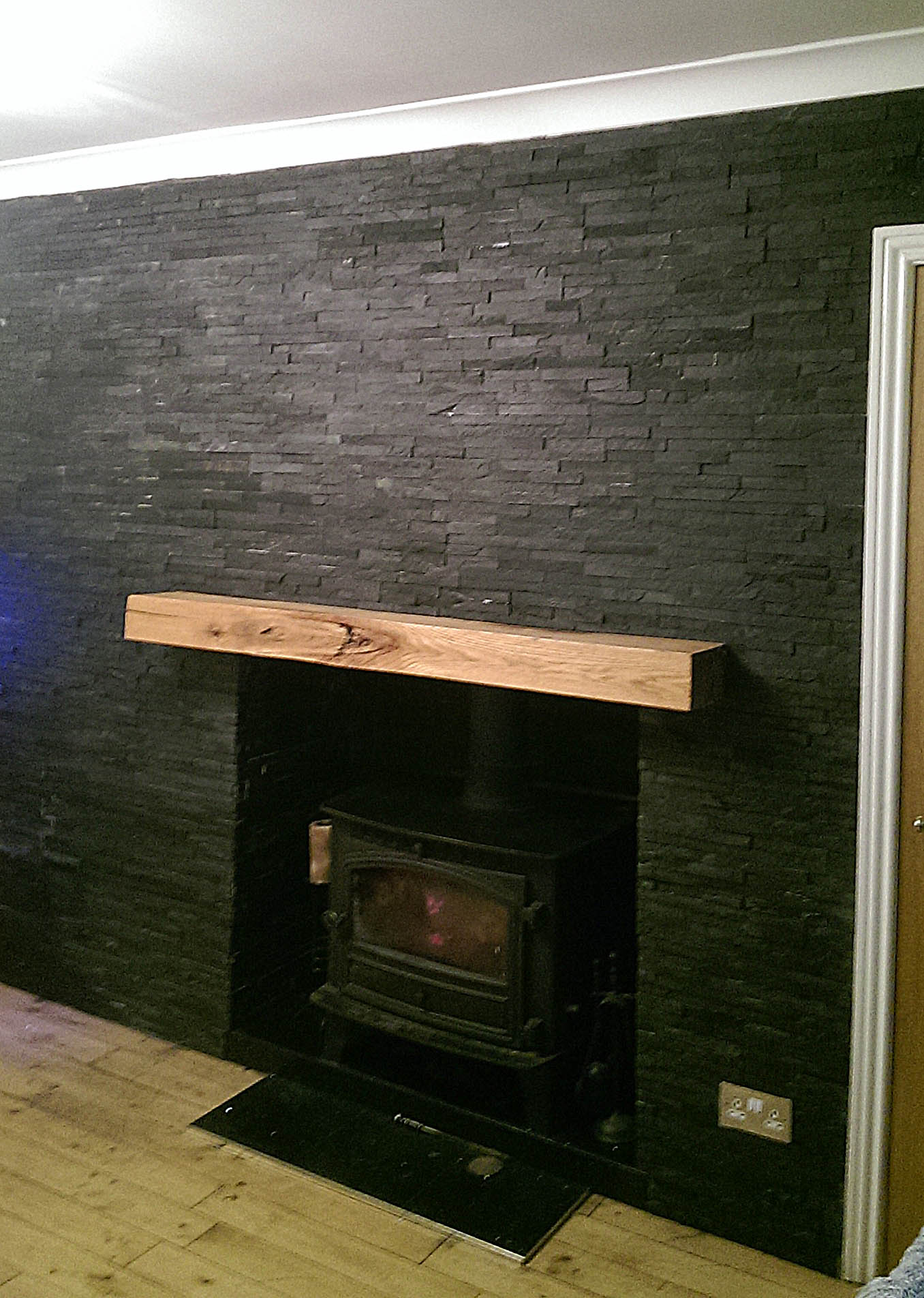 Black split-face slate feature wall around a wood-burning stove with an oak beam