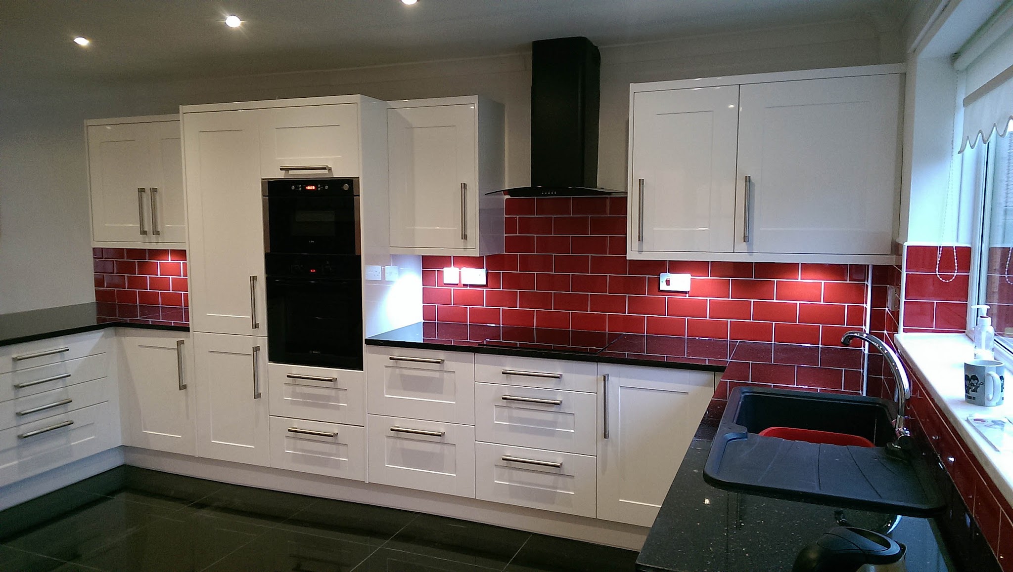 White shaker kitchen with a red brick-pattern tiled splashback and black worktops