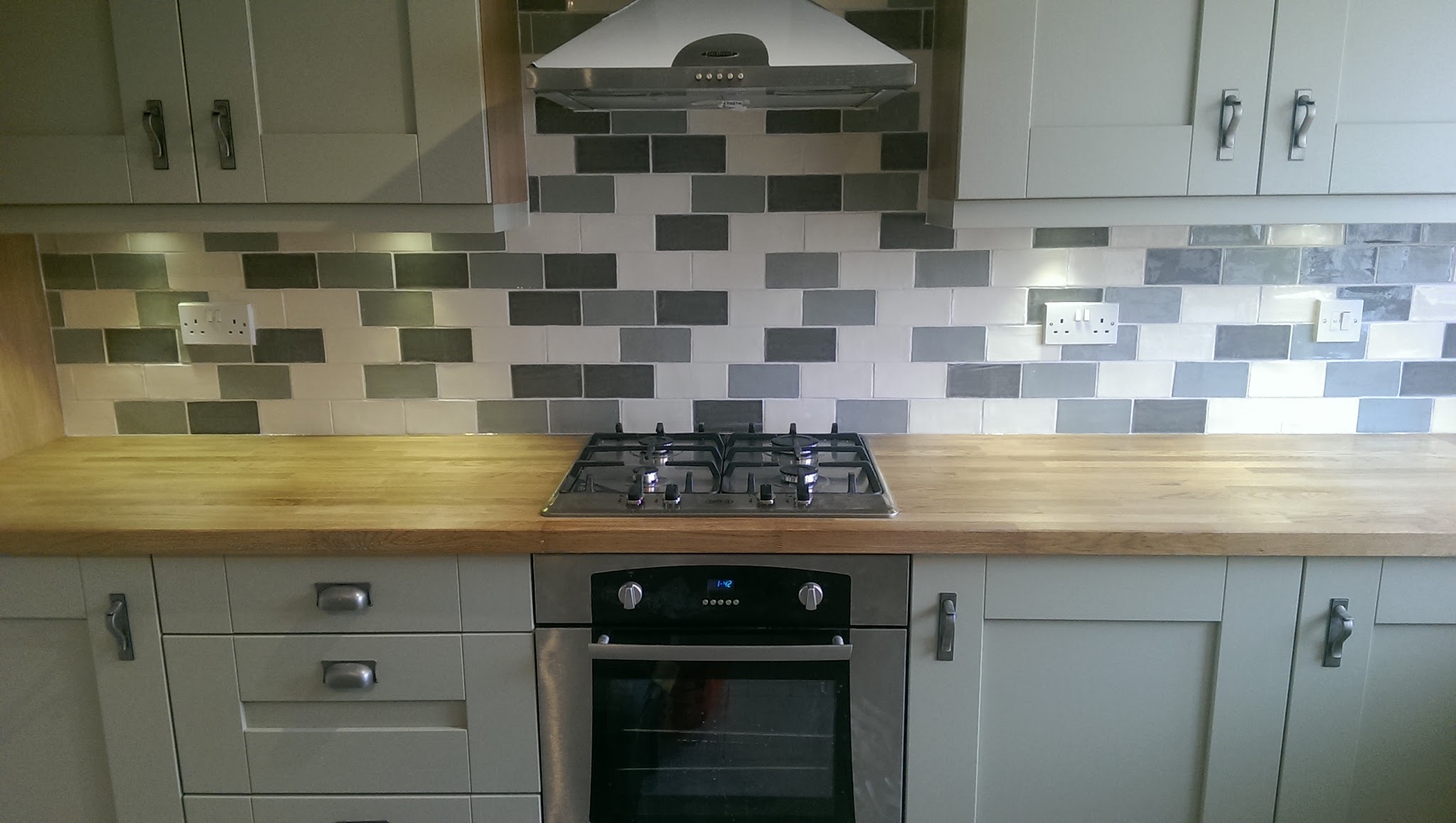 Grey and white brick-bond splashback behind a gas hob and oak worktop