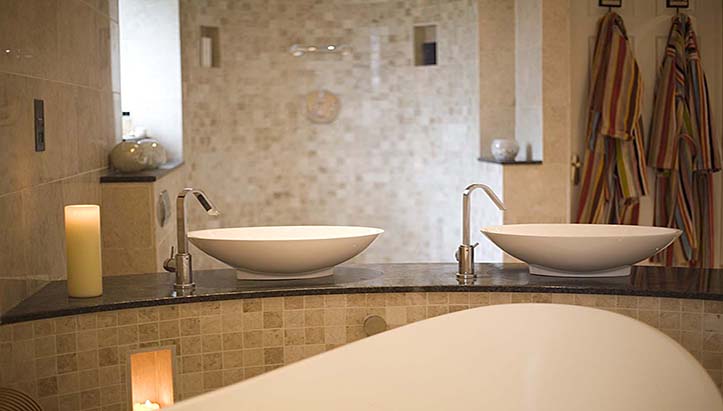 Twin vessel basins on a granite top above a curved mosaic plinth, lit by candles