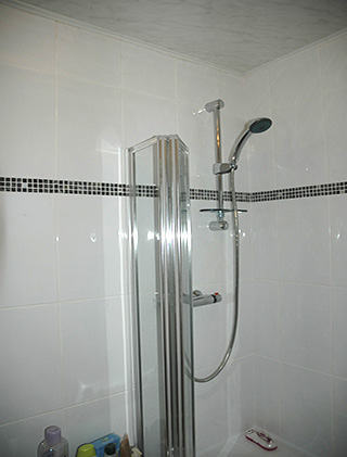 New shower over the bath with white tiles and a black mosaic border